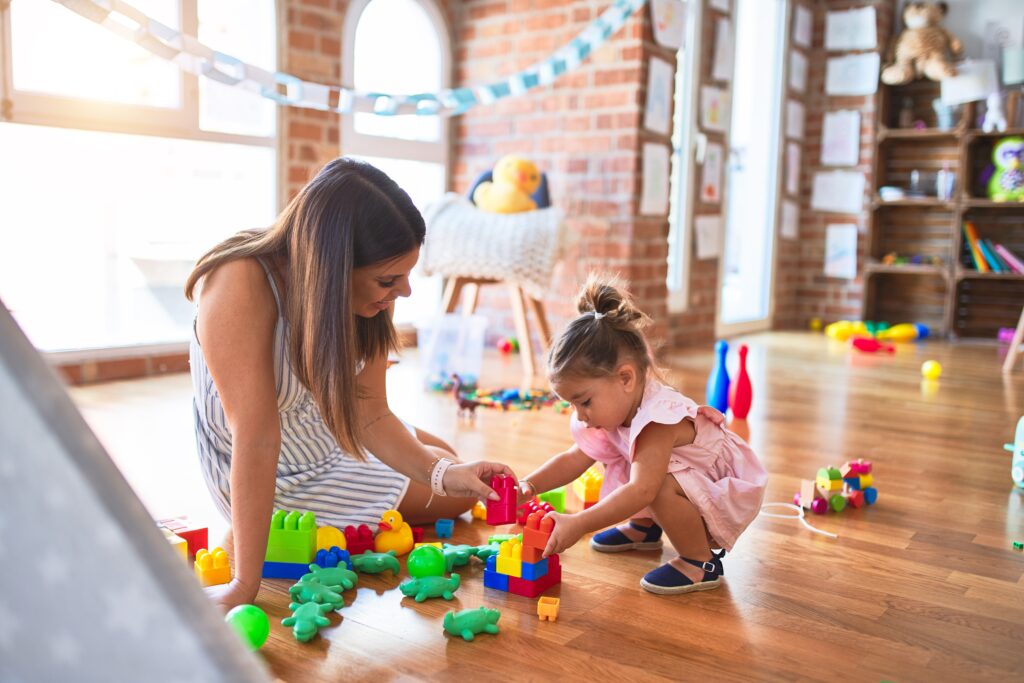 ABA Therapist sitting on the floor working with a young girl using building blocks